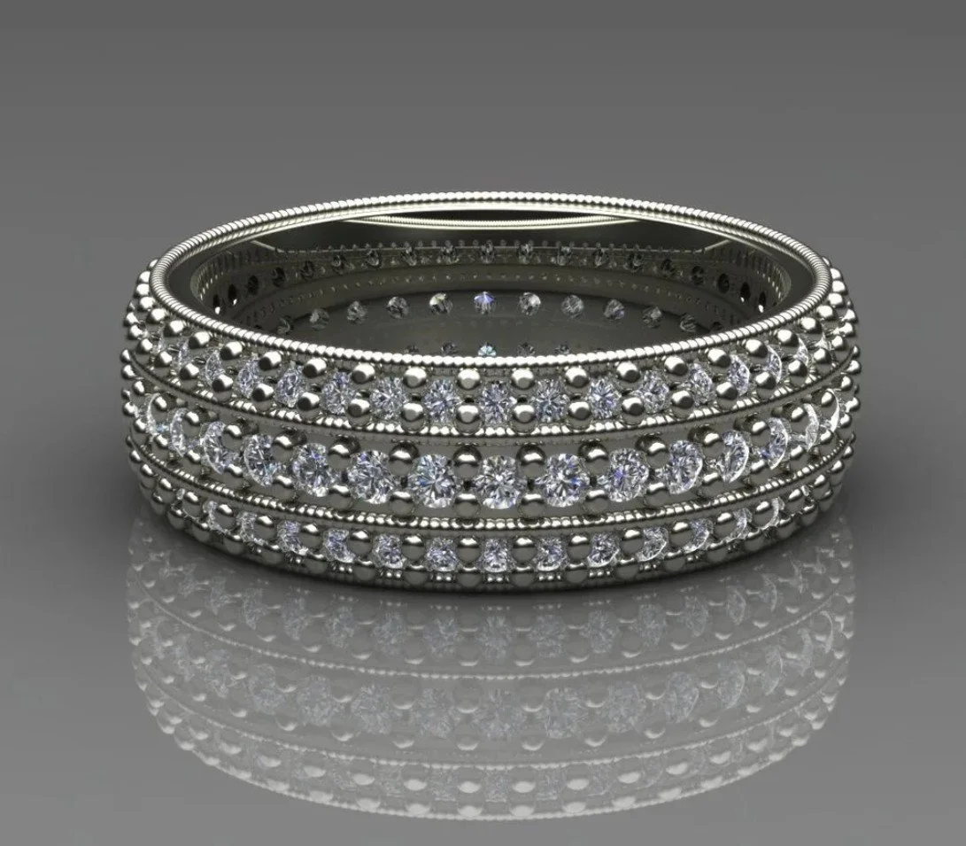 A stack of four silver rings with embedded small clear gemstones, sitting on a reflective gray surface.