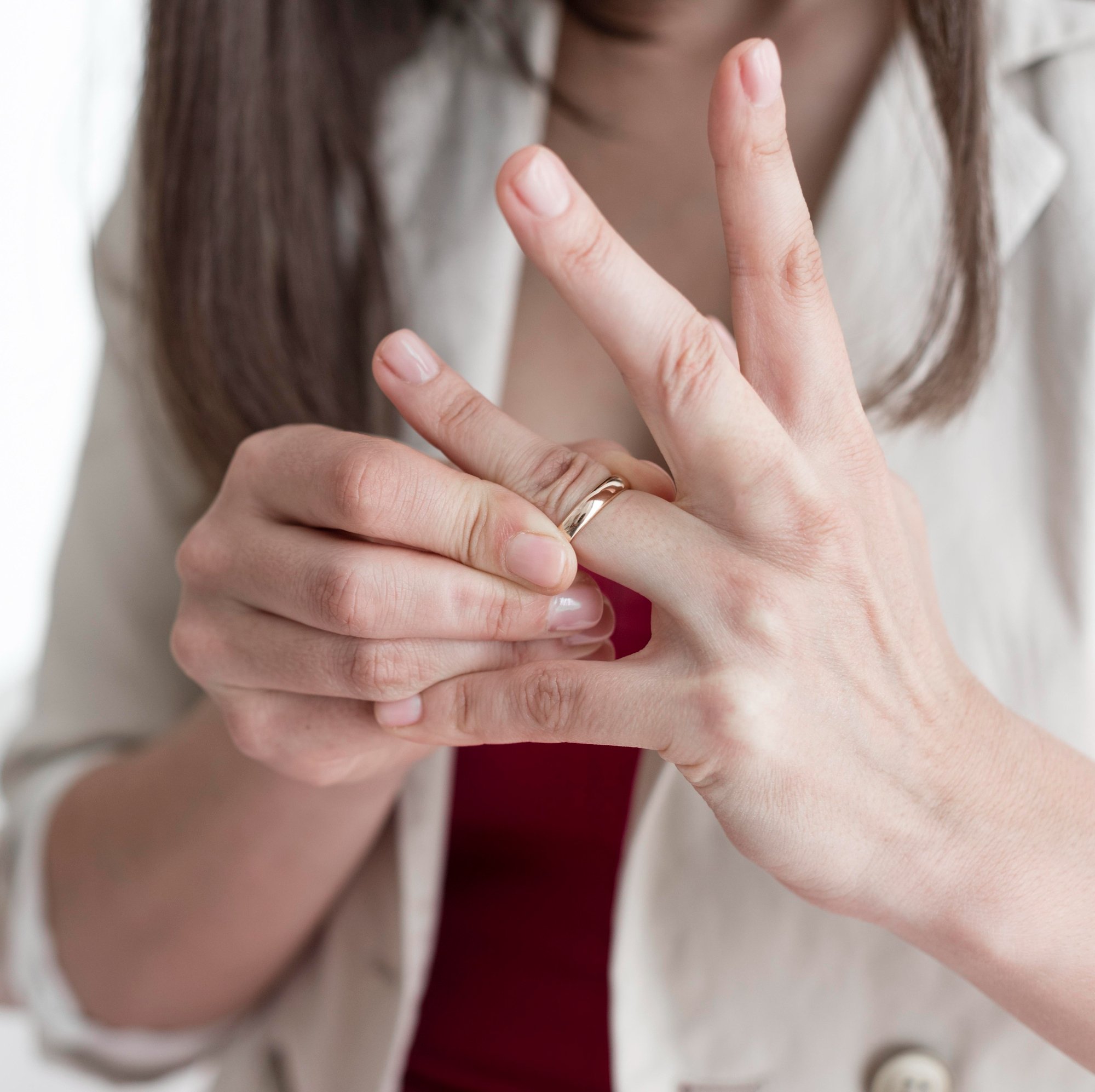 Close-up of a person with long dark hair making an 'OK' gesture with their hand, fingers forming a circle. The person is wearing a white blazer and a red shirt.