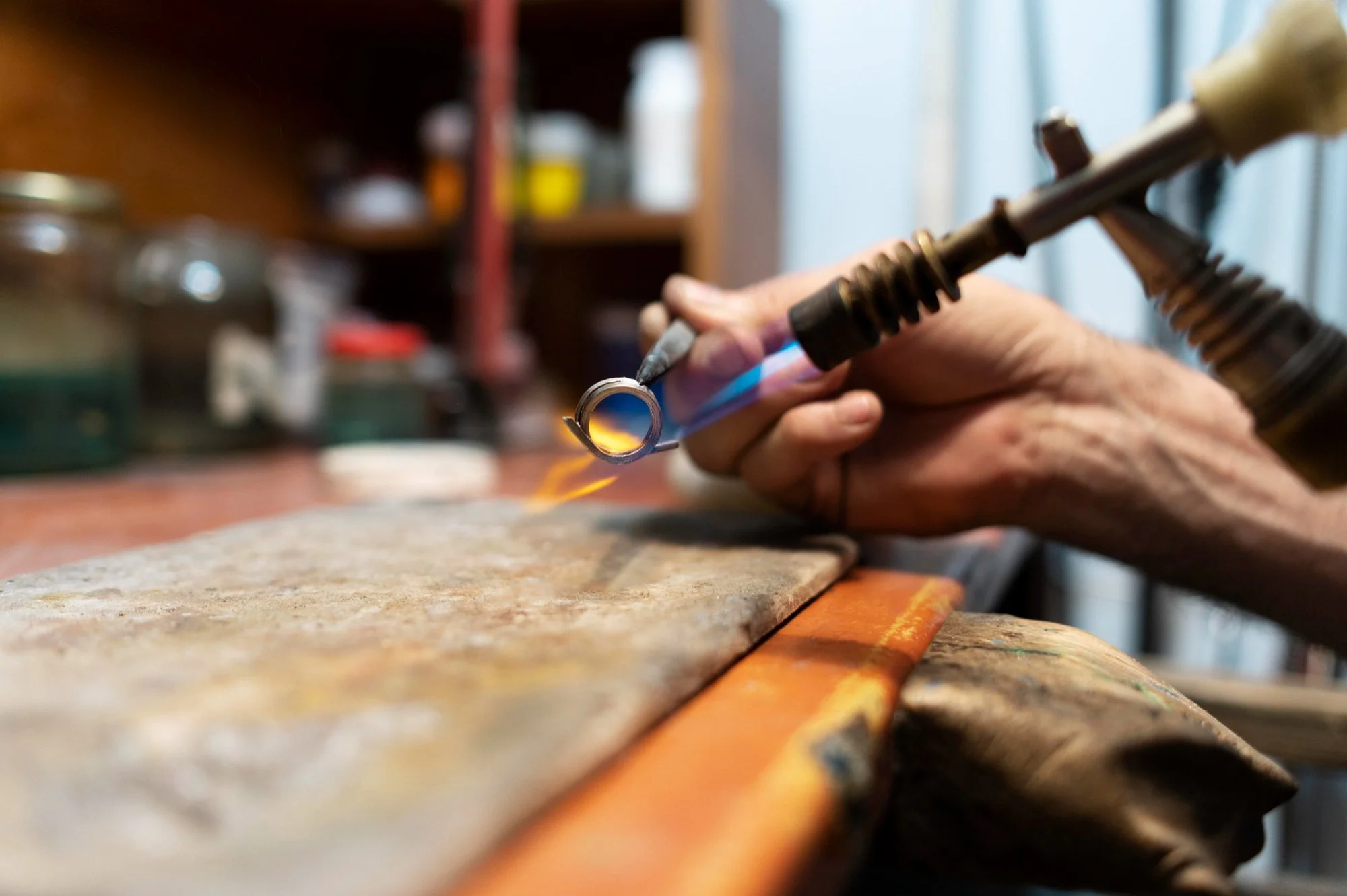 A person uses a blowtorch to melt or shape metal in a workshop or craft setting.