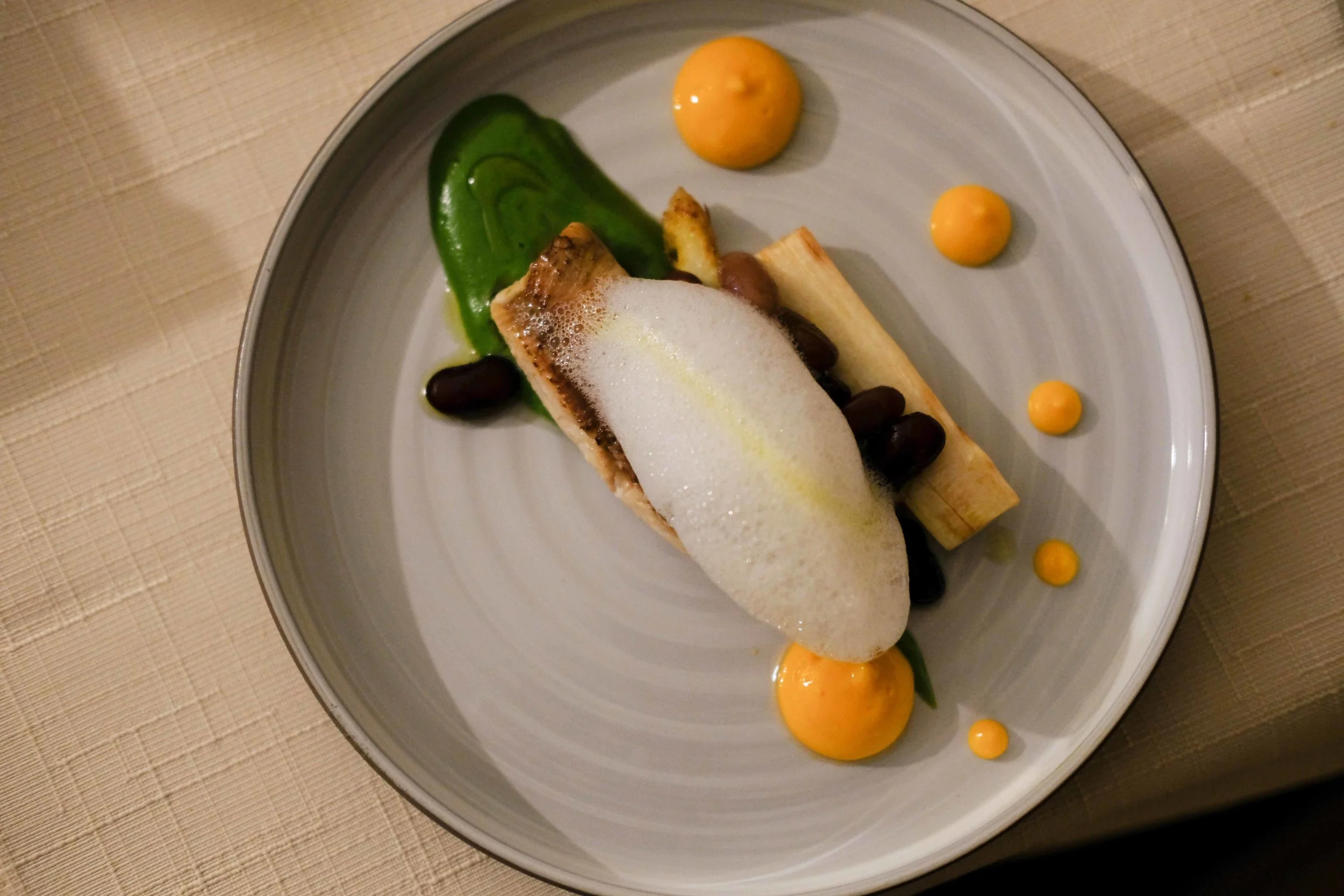 River trout on prosciutto and covered with lemon foam, white asparagus with sweet brown beans, green asparagus puree and dots of puree of carrot.