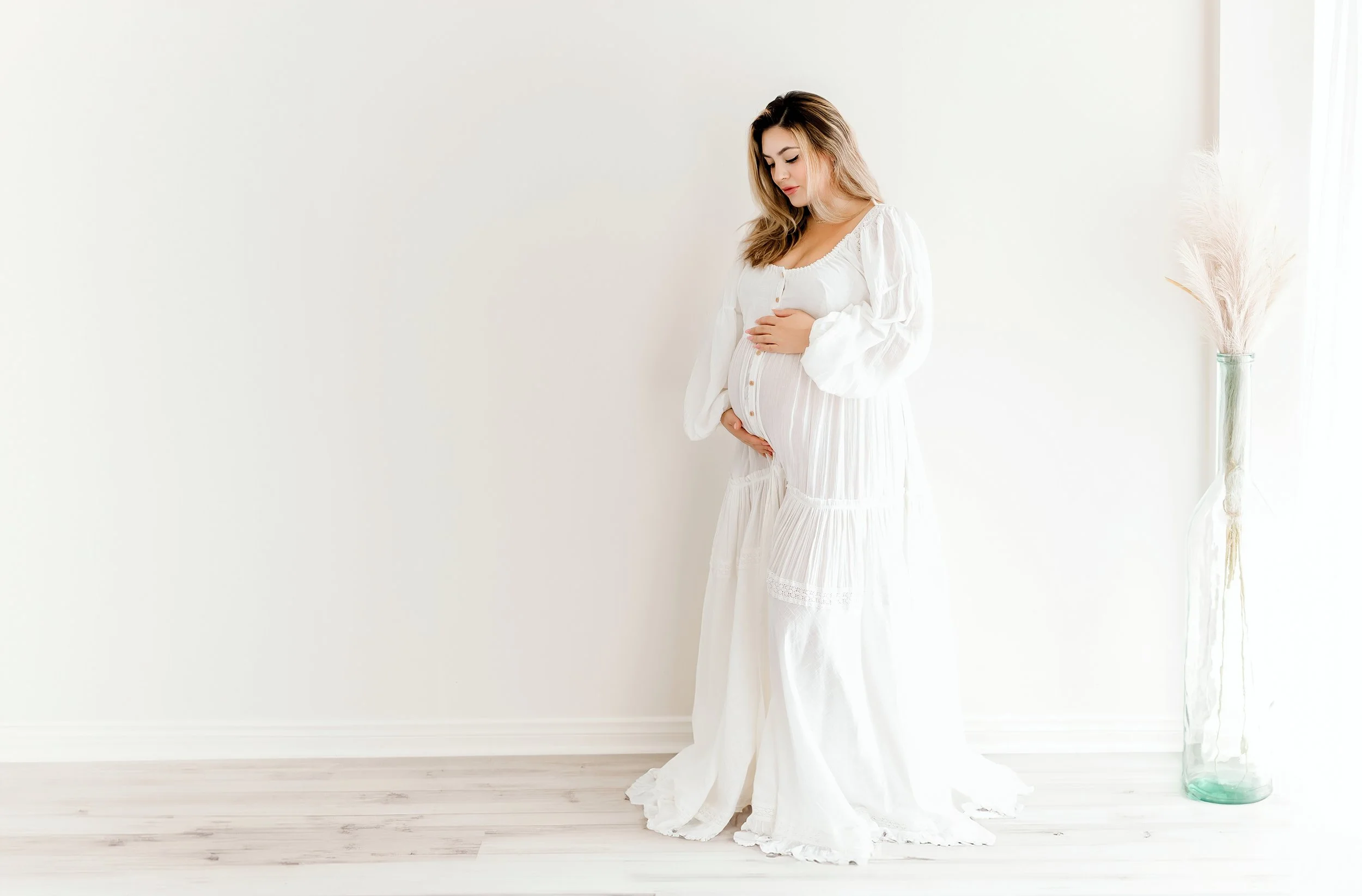 pregnant mom posing for maternity photos in a white dress made from reclamation dress company in photo studio
