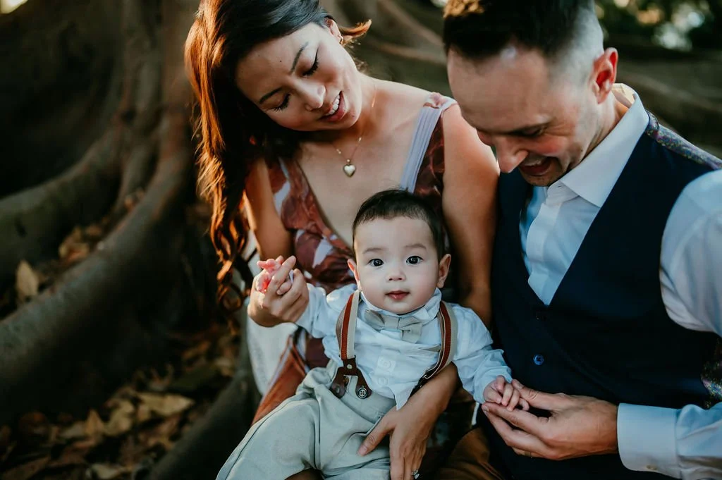 Parents holding their baby sitting on the root of a banyan tree