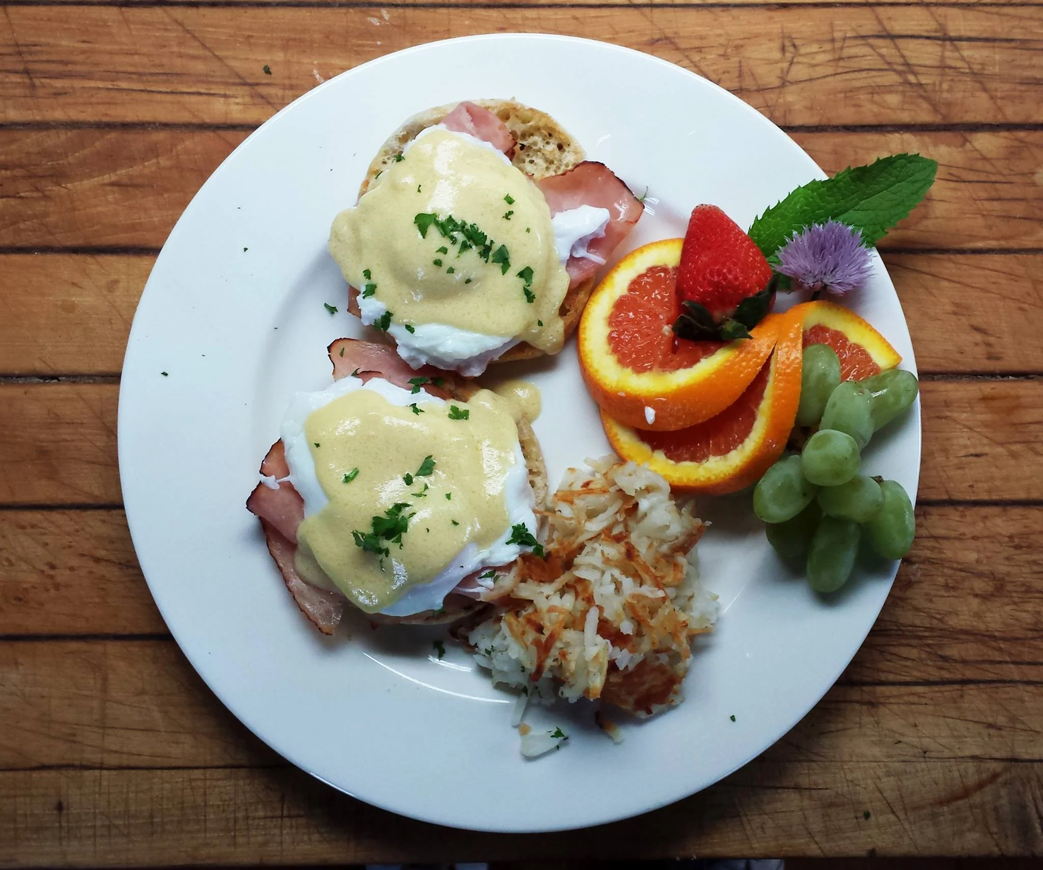 A breakfast plate of Eggs Benedict with Hash Browns and Fresh Fruit