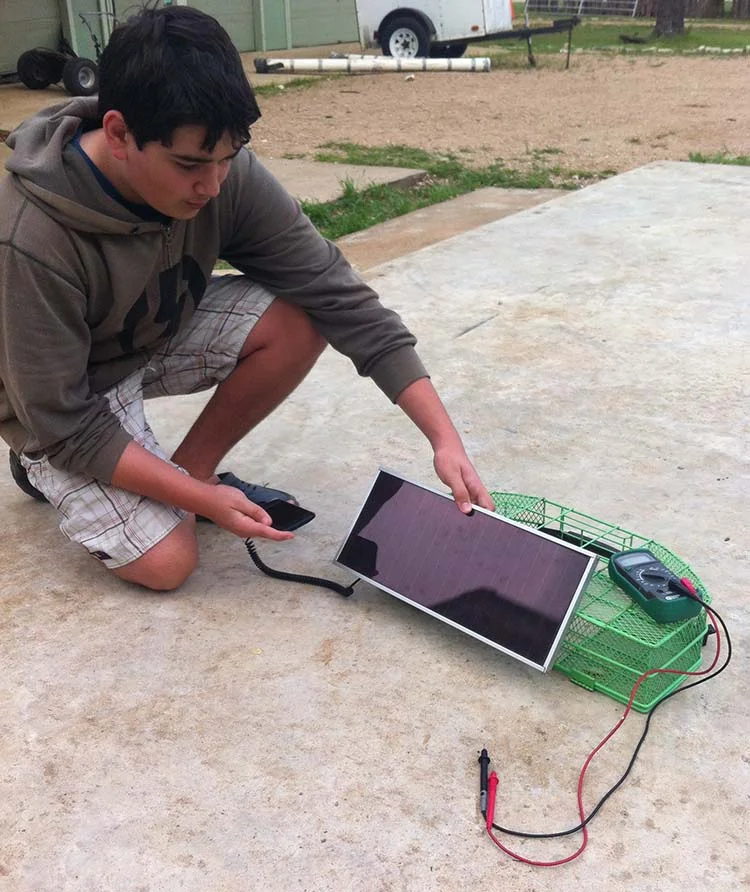 Cainan working on a solar-powered phone charger from a hacked phone charger that plugs into a cigarette lighter and a solar panel from a garage sale.