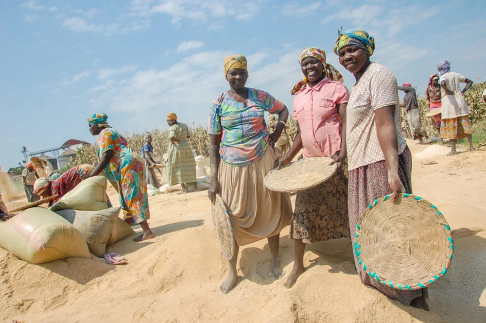 Esther (center) works alongside Martha (right) to sift chenga (broken rice) in Doko. 
