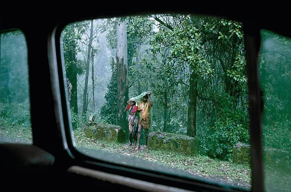 photograph of two people standing in the rain as viewed from inside a car window