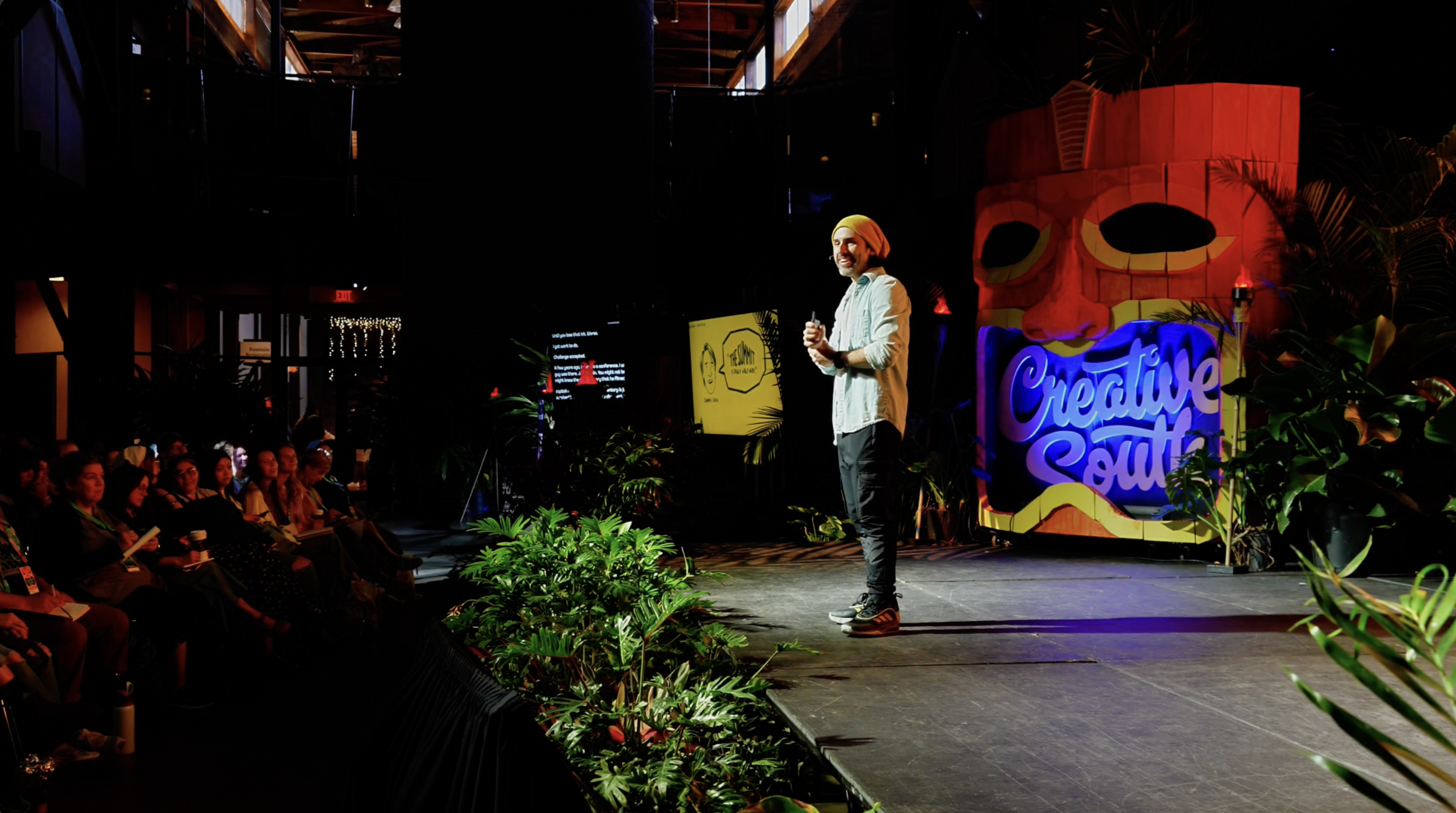 Alejo on a stage at a creative conference, the decoration resembles a jungle, he's smiling and the audience, too.
