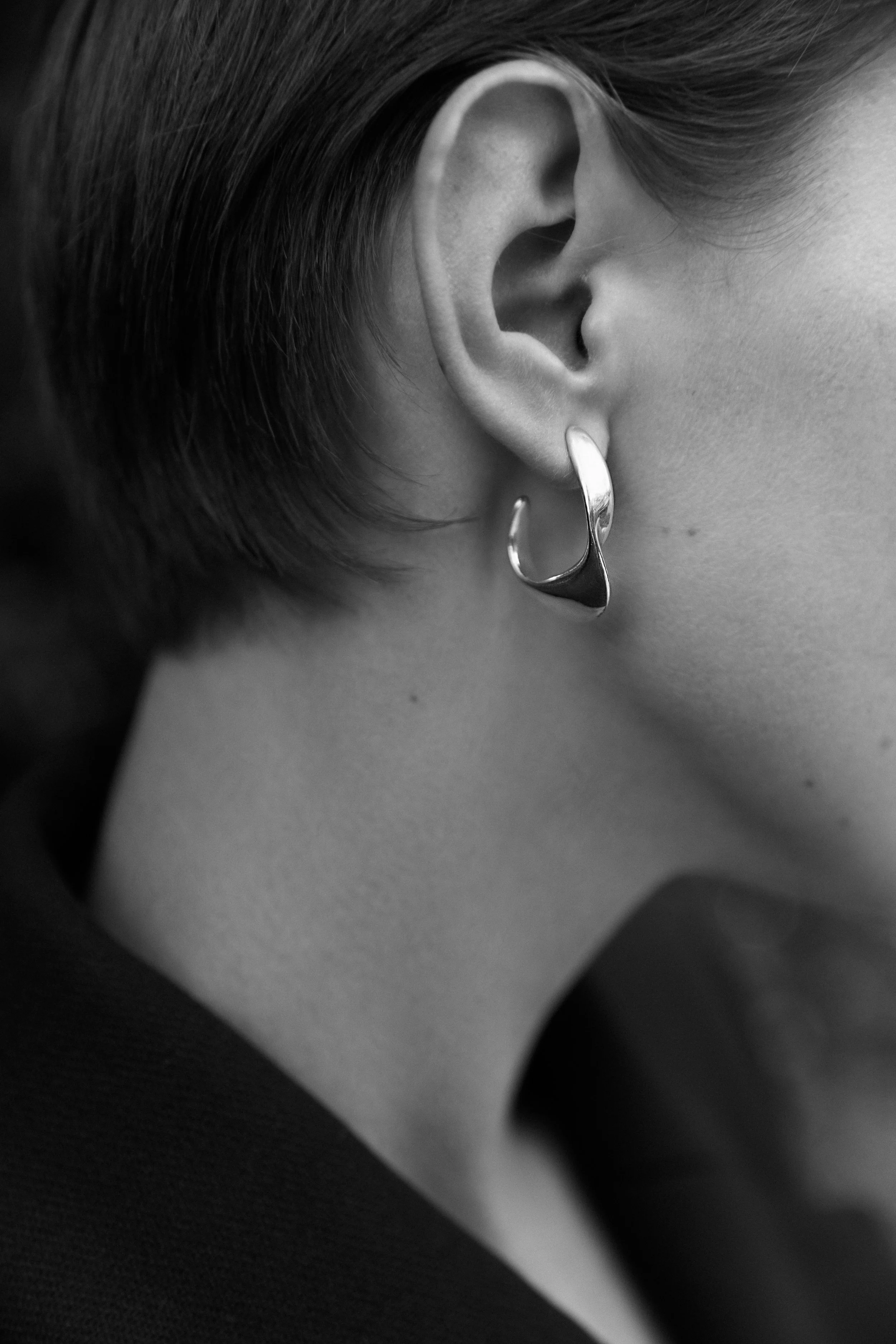 Close-up of a person's ear with a shiny, abstract-shaped earring, taken in black and white.