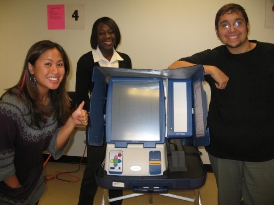Student poll workers pose with a touchscreen voting machine. Photo by Paulina Mysliwiec.