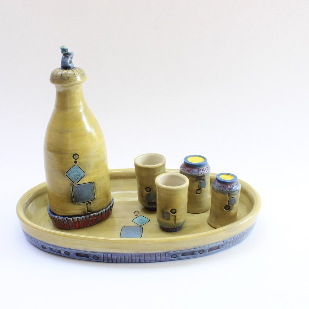 A yellow ceramic liquor decanter with four matching cups on a matching tray.