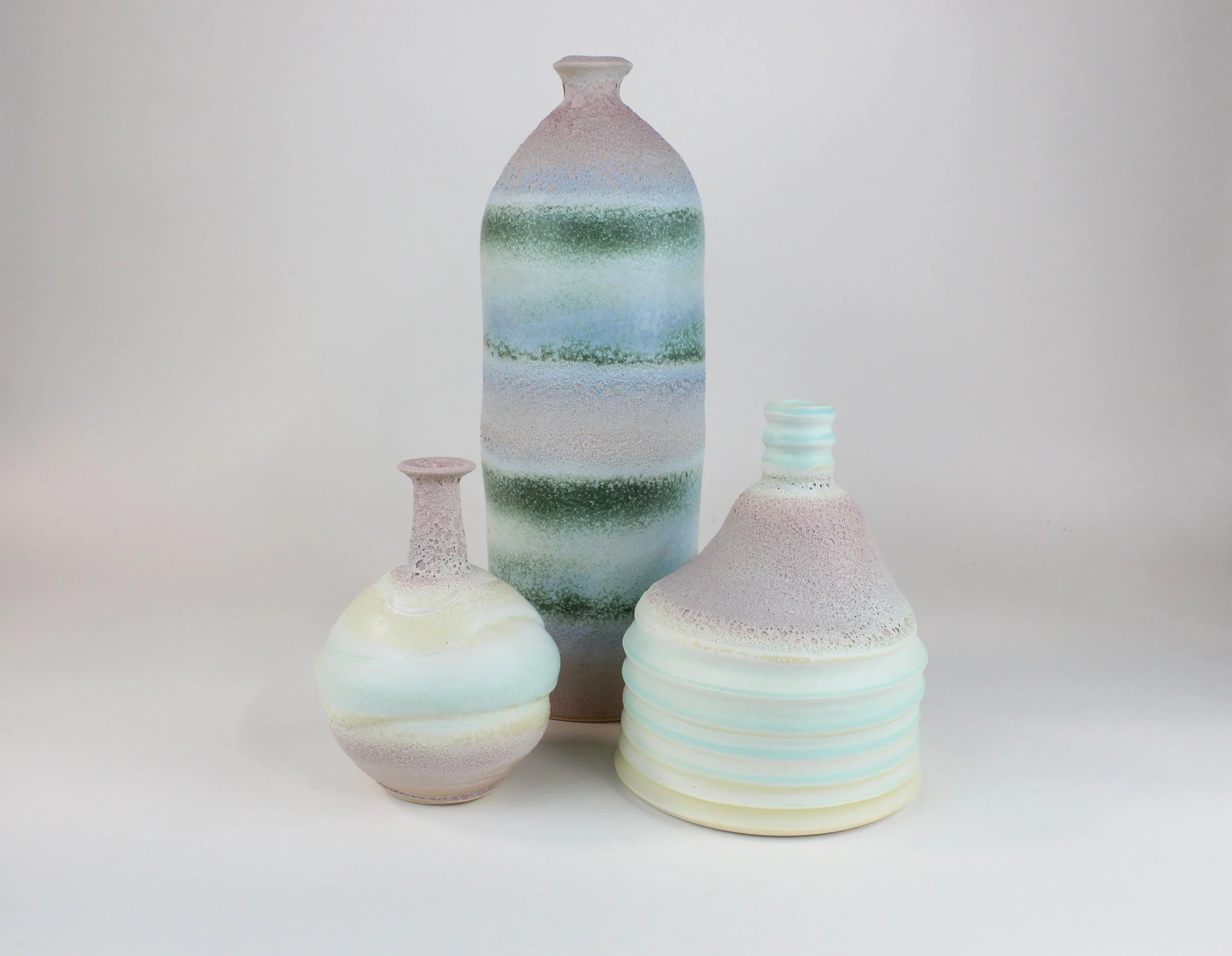 A collection of colorful ceramic vases with textured surfaces, featuring pastel shades of pink, green, blue, and white, arranged on a plain white background.
