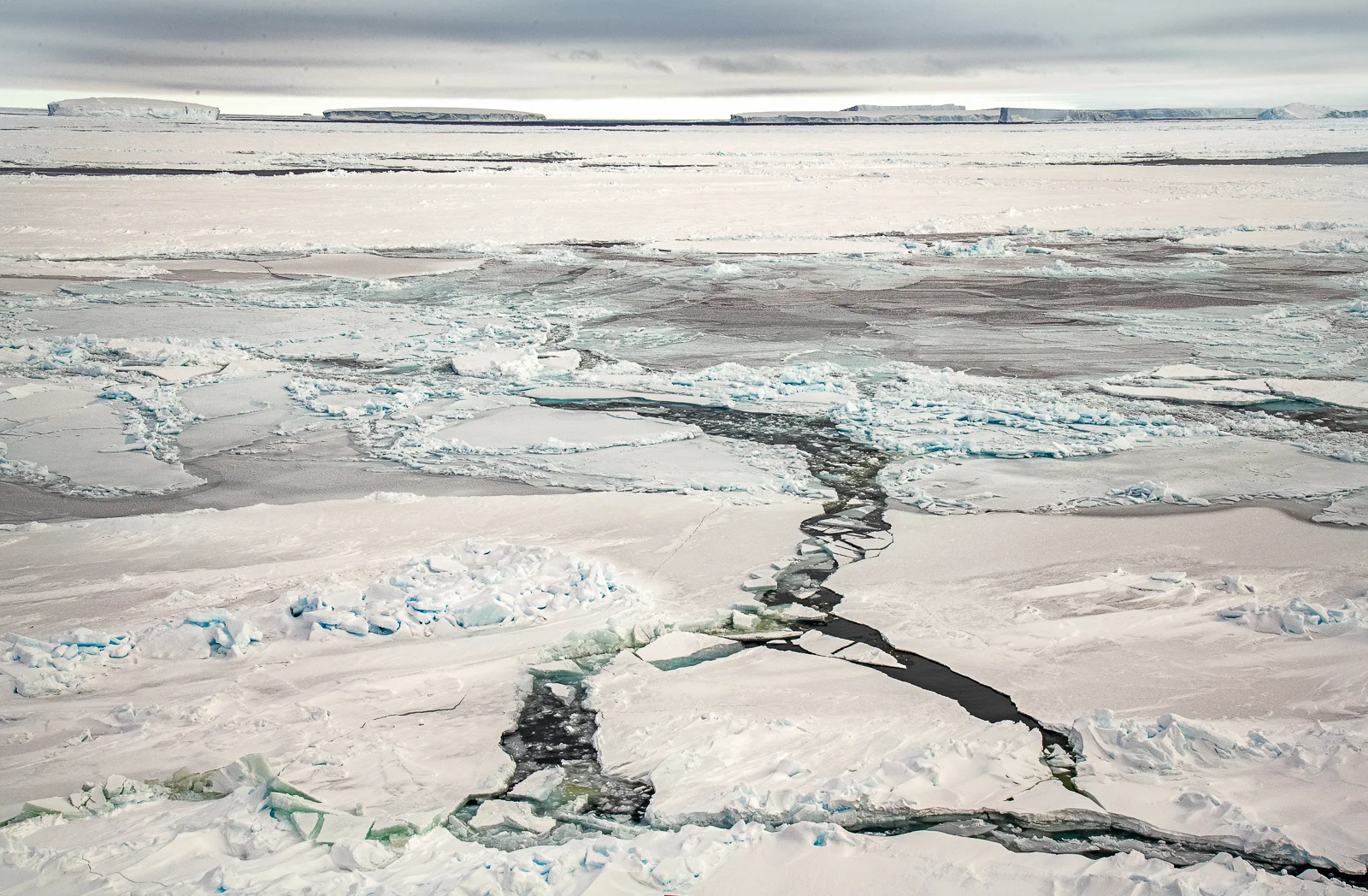 Antarctic Sea Ice Landscape with Fractures and Icebergs on the Horizon
