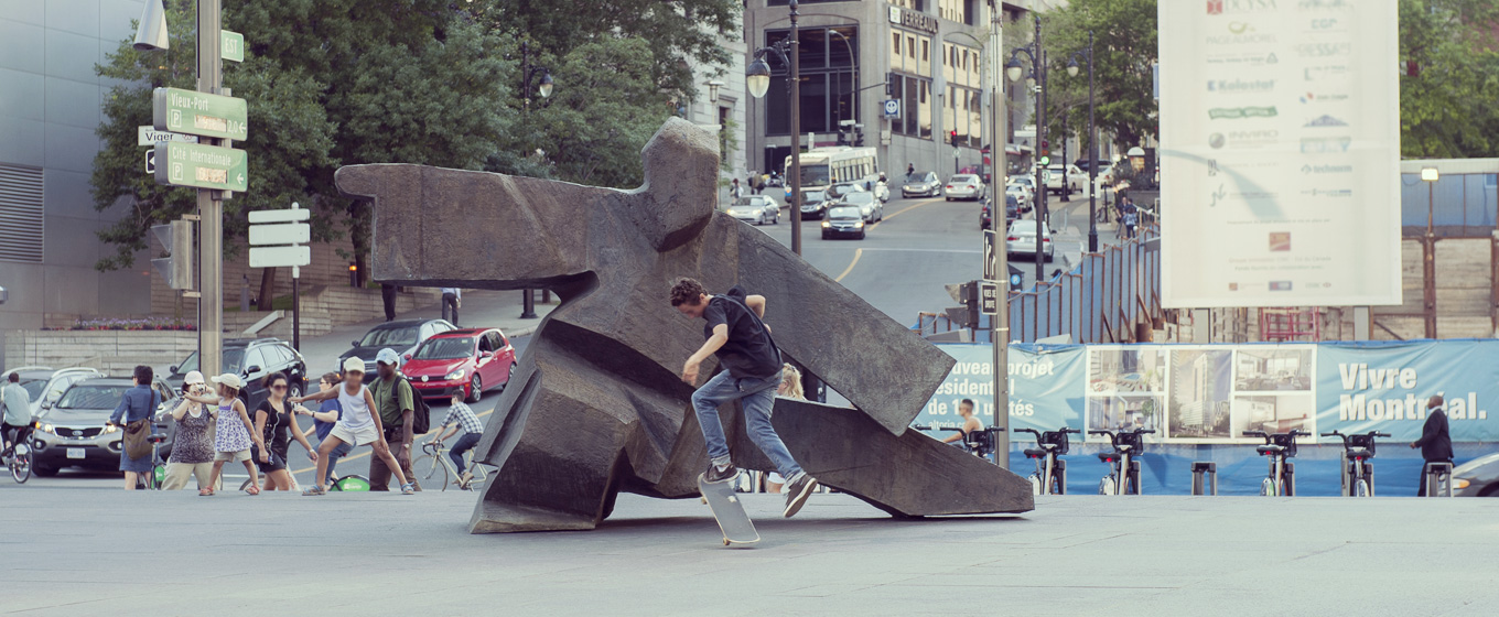 Un adolescent fait du skateboard devant Taichi Single Whip (1985) de Ju Ming, qui est installée au square Victoria, alors qu’un enfant imite la pose de la sculpture à l’arrière-plan, à gauche. © Denise Caron