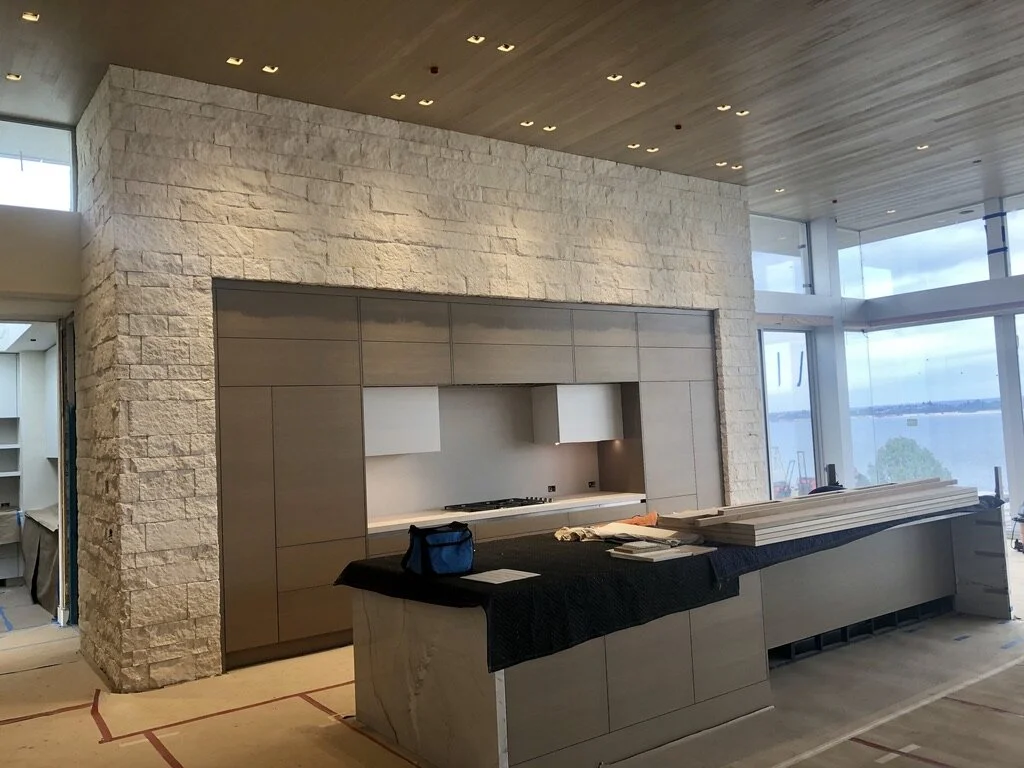 Modern kitchen with a central island, stone wall, and floor-to-ceiling windows overlooking water.