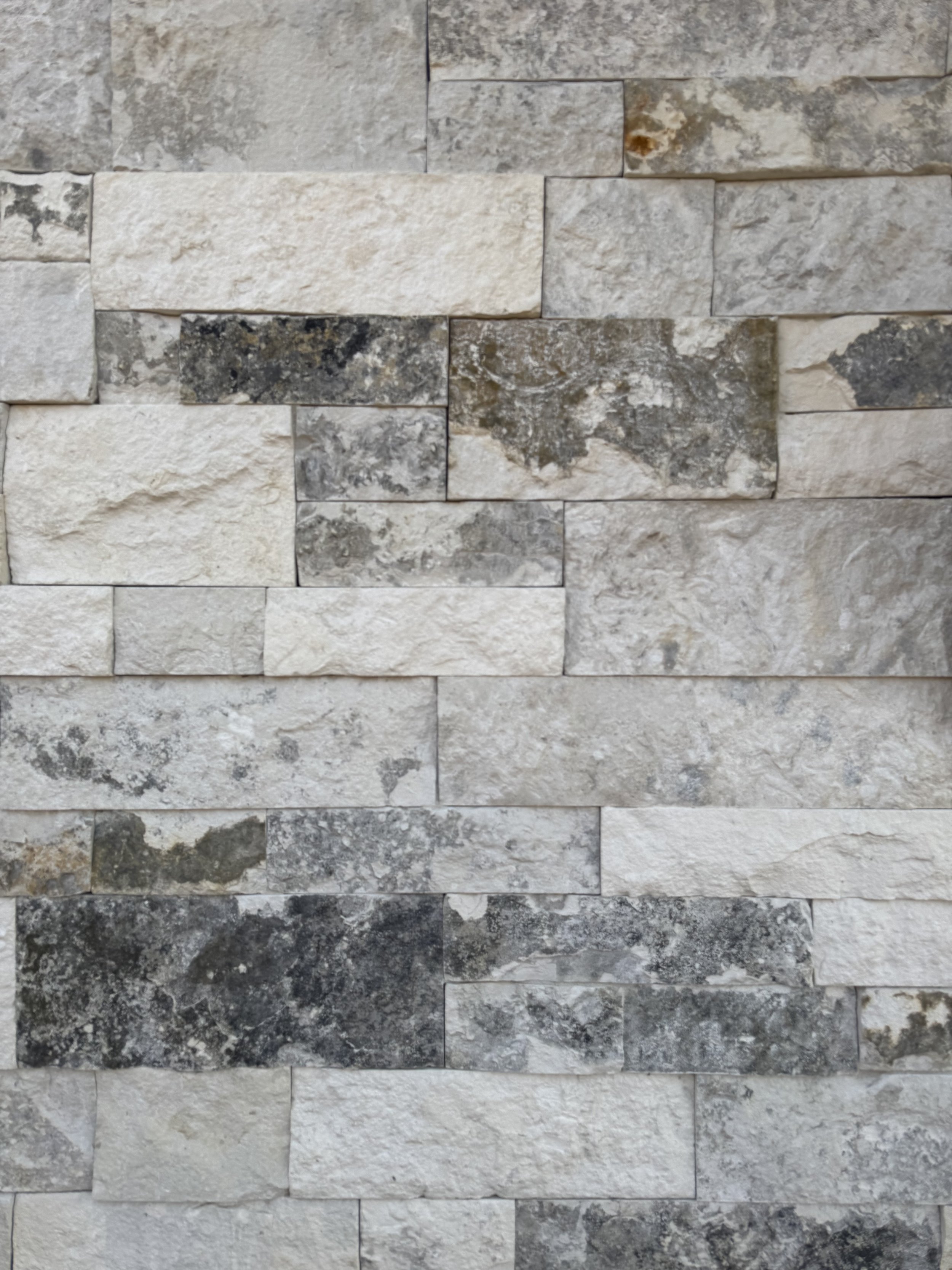 Close-up of a textured stone wall with rectangular stones in shades of gray, cream, and beige.
