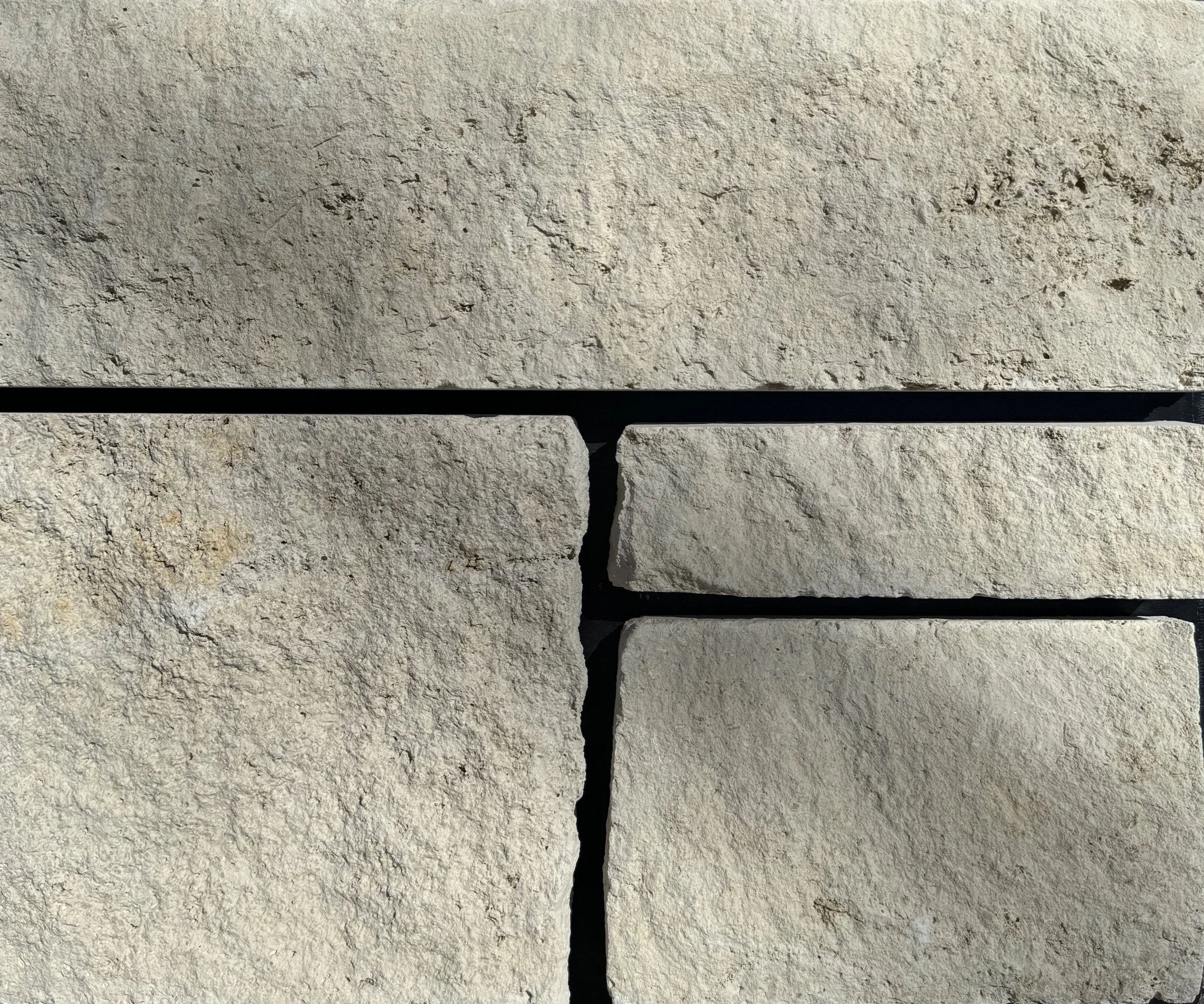 Close-up of beige and tan stone bricks with black grout lines.