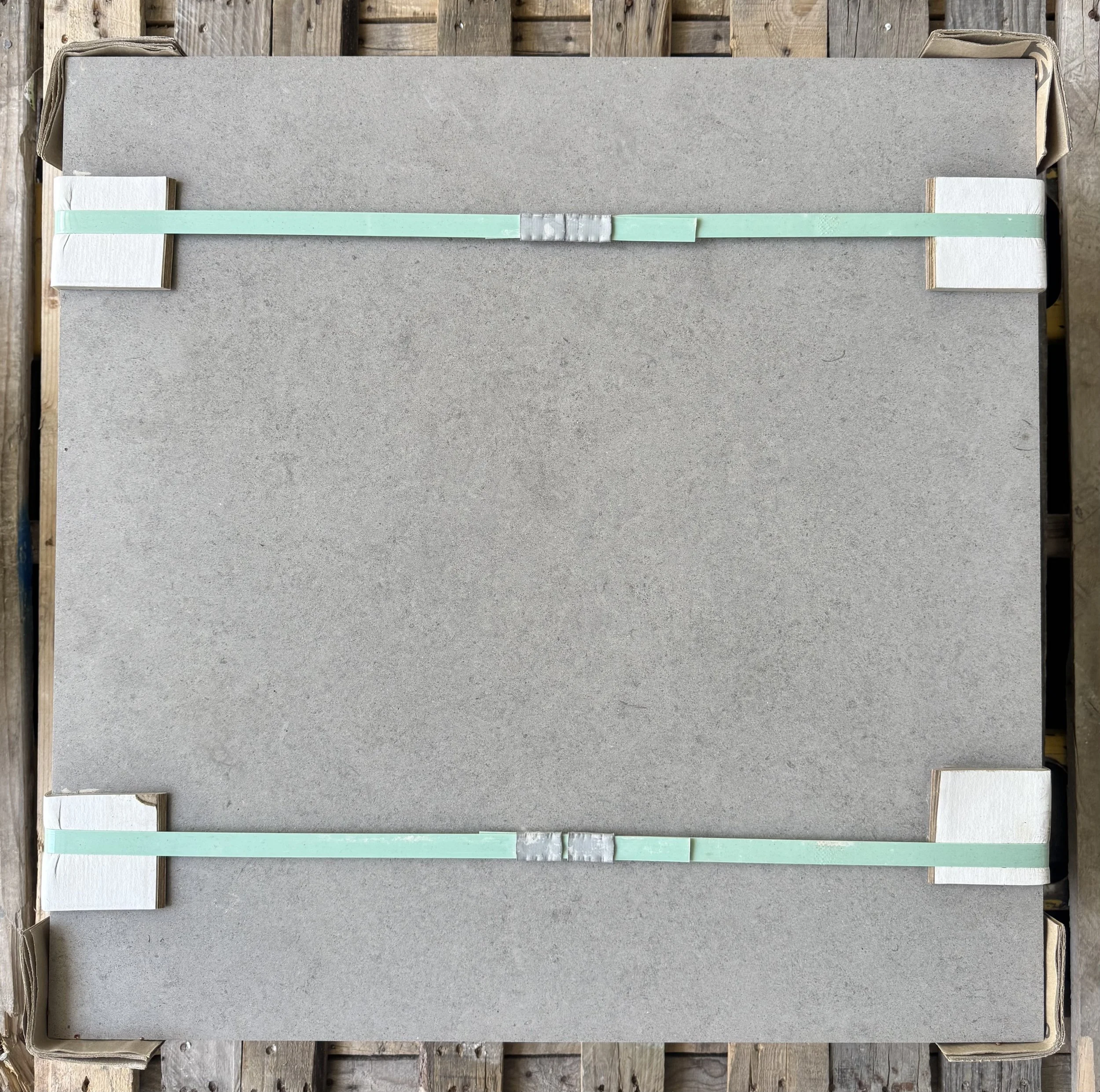 A large gray flat tile with white foam spacers and light green plastic tiles along the edges, placed on a wooden surface.