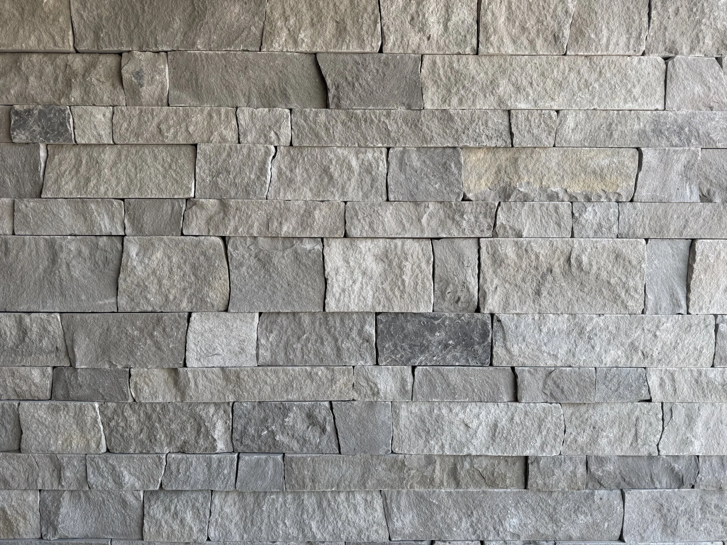 Close-up of a stone wall made of rectangular, textured, light gray stones arranged in horizontal rows.