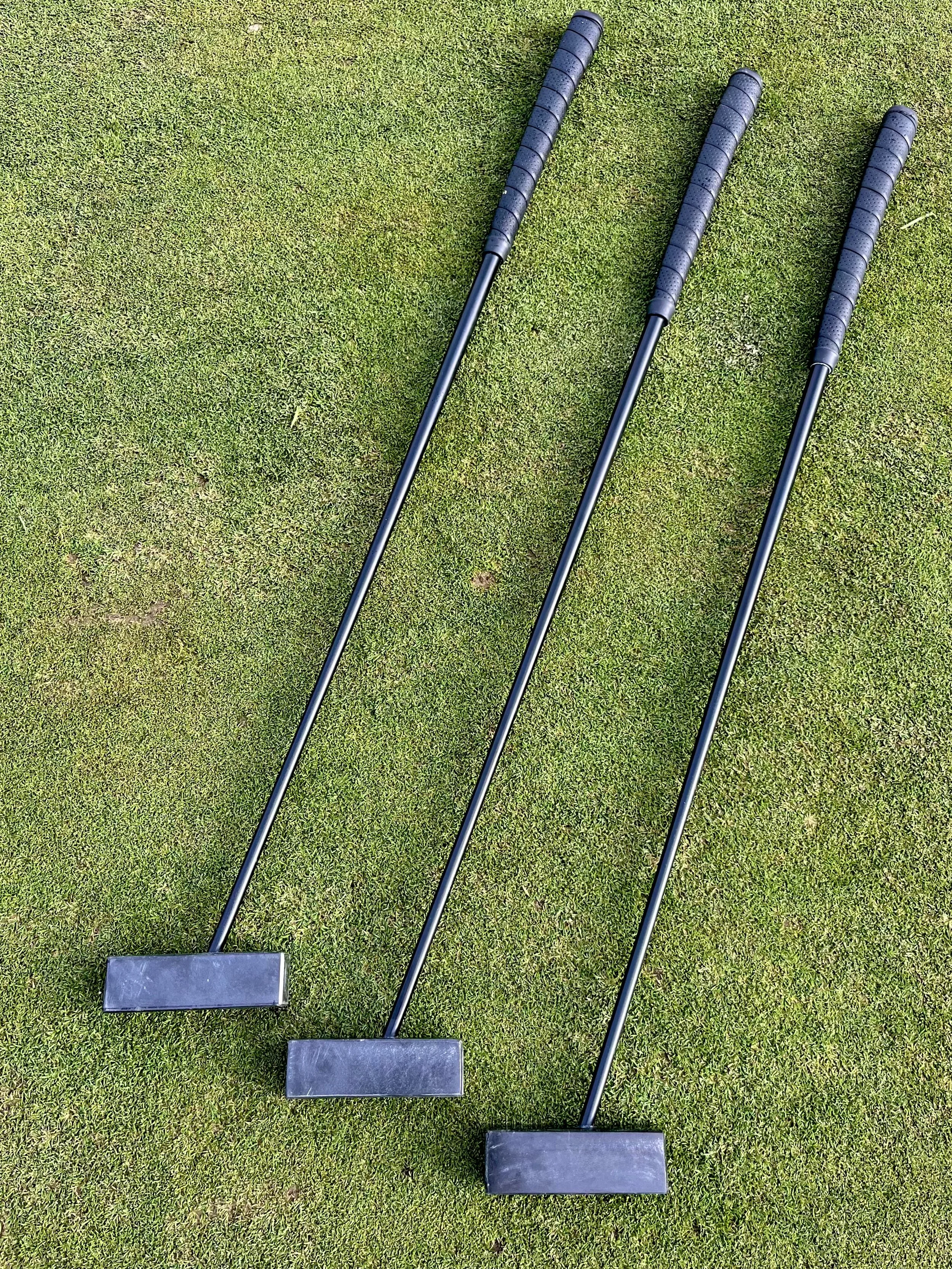 Three golf putters laying on a grassy golf green.