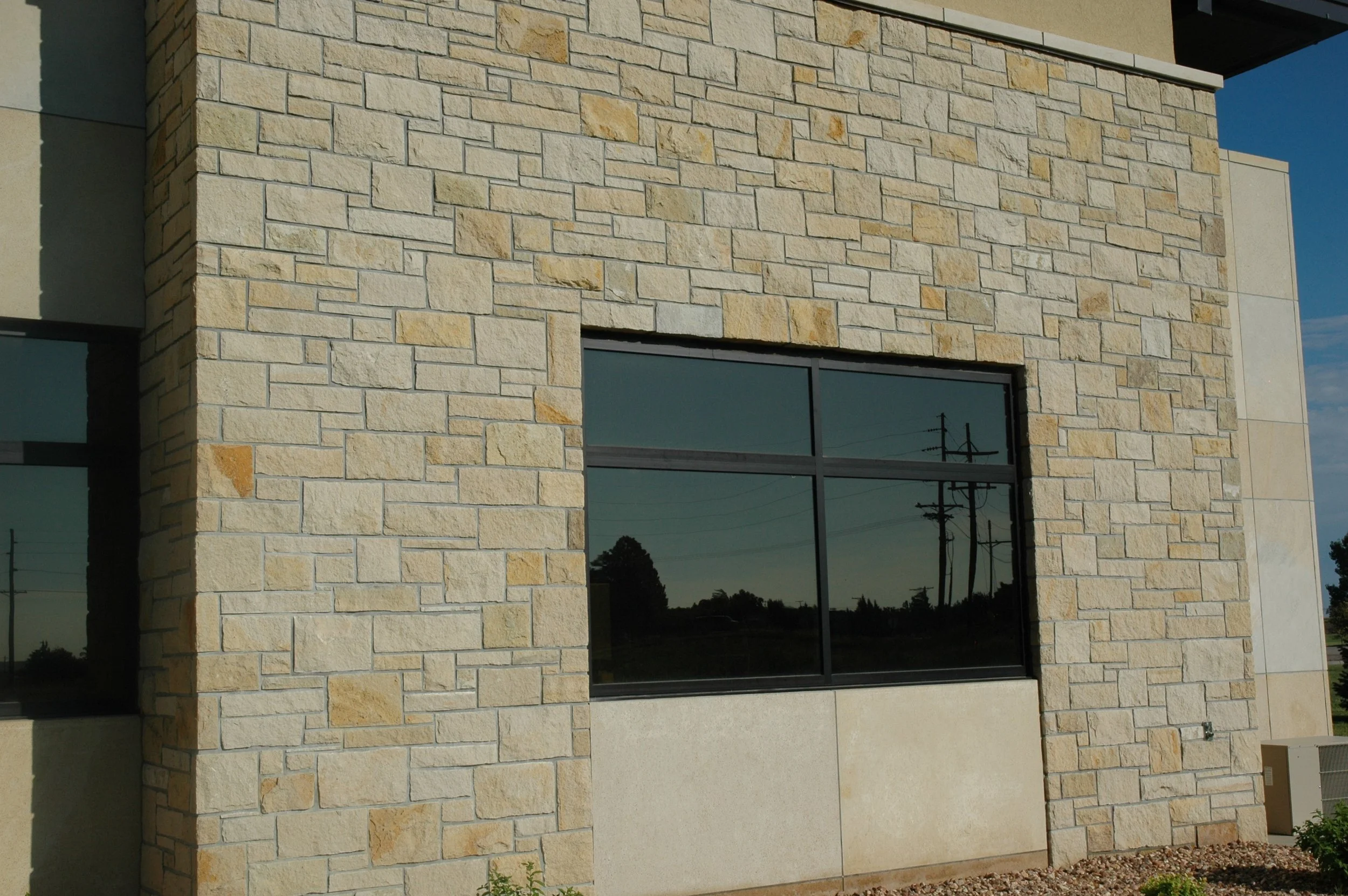 Exterior of a building with a wall made of beige and tan bricks, featuring a large rectangular window with reflective glass.