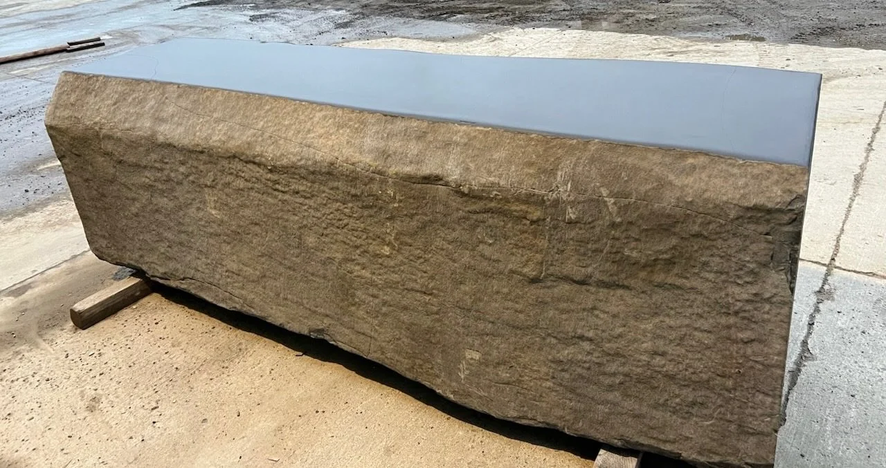 A large stone with a smooth, polished top surface resting on wooden supports, outdoors on a concrete surface.