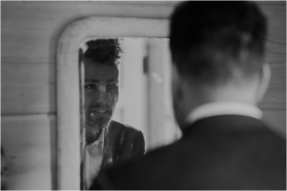 groom looking into mirror getting ready before wedding ceremony