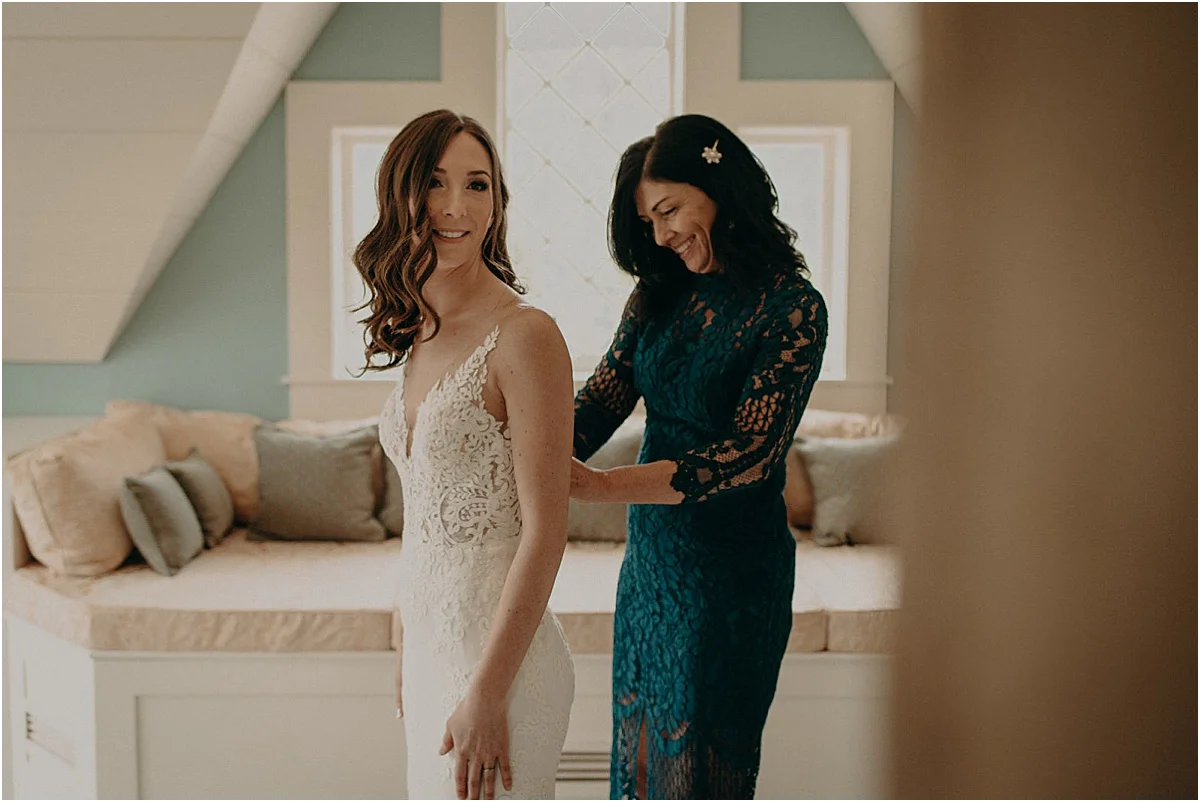 bride and mother of the bride putting on white wedding dress