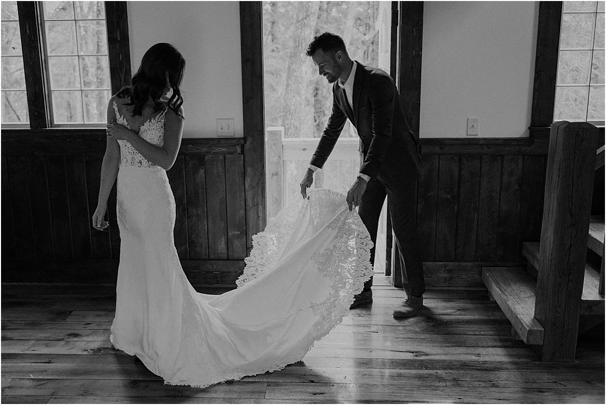 groom helping bride with her white wedding dress train