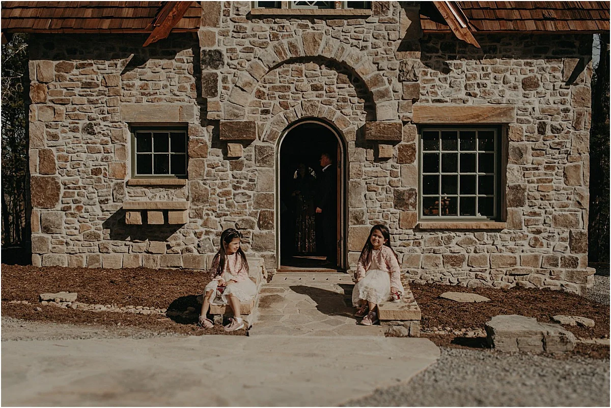 two girls sitting on the ground in front of brick cottage