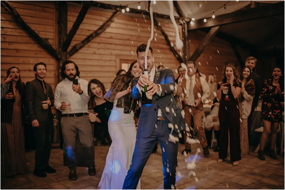 bride and groom popping champagne with guests at wedding reception