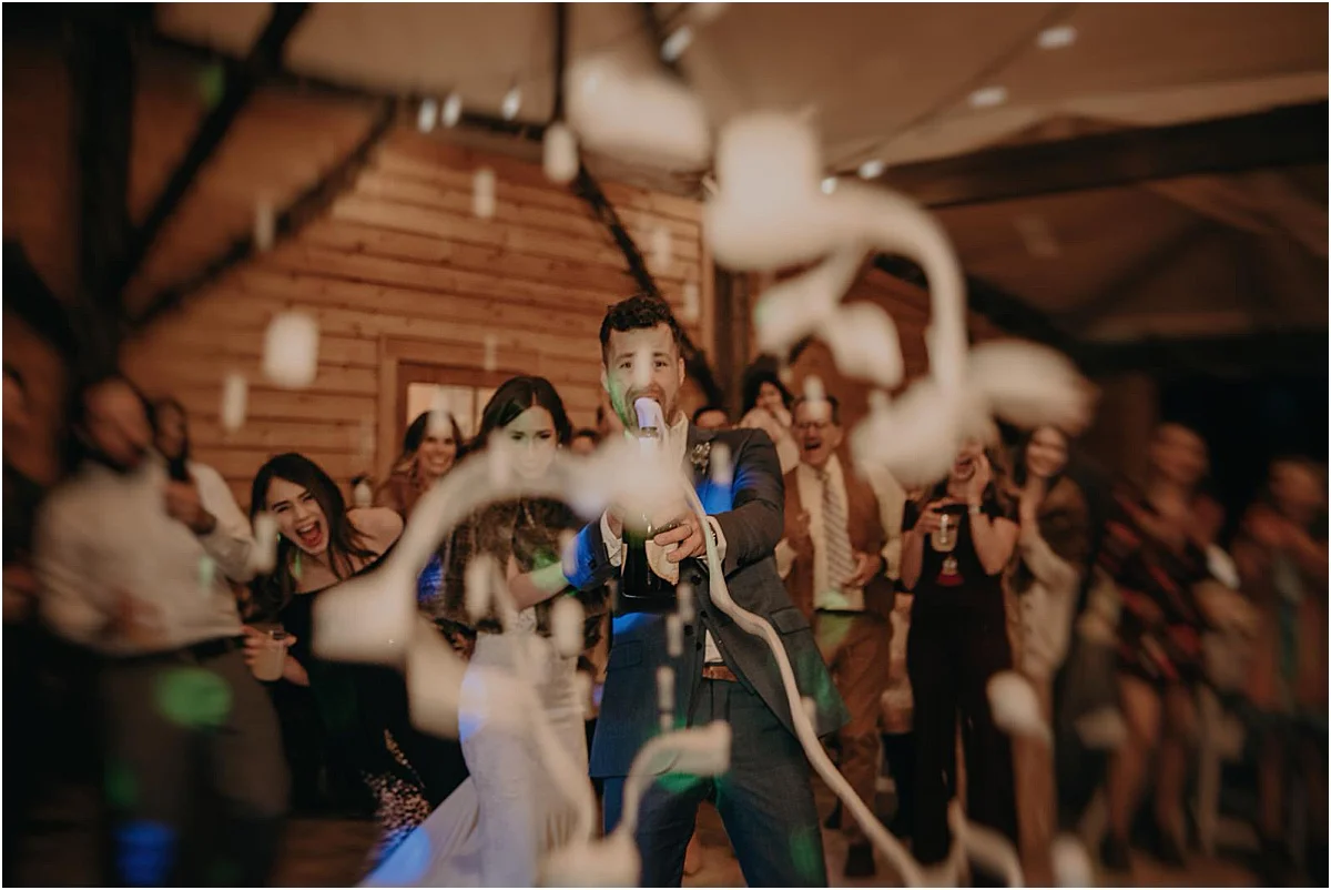 bride and groom popping champagne at camera during wedding reception