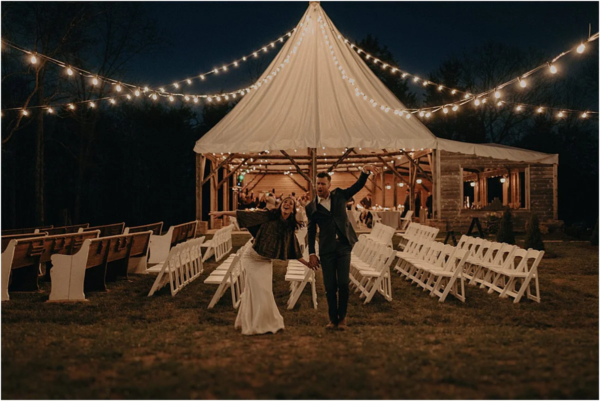 bride and groom celebrating in front of tent and lights at night