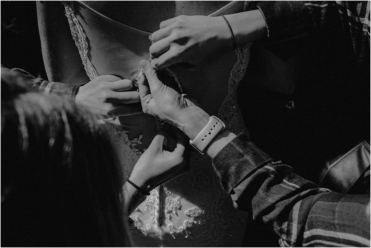 bridesmaids helping bride button wedding dress before ceremony