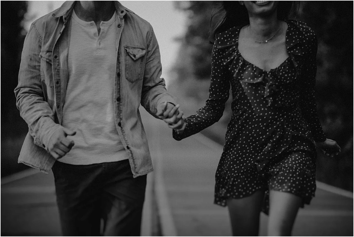 engaged couple running down the road while holding hands