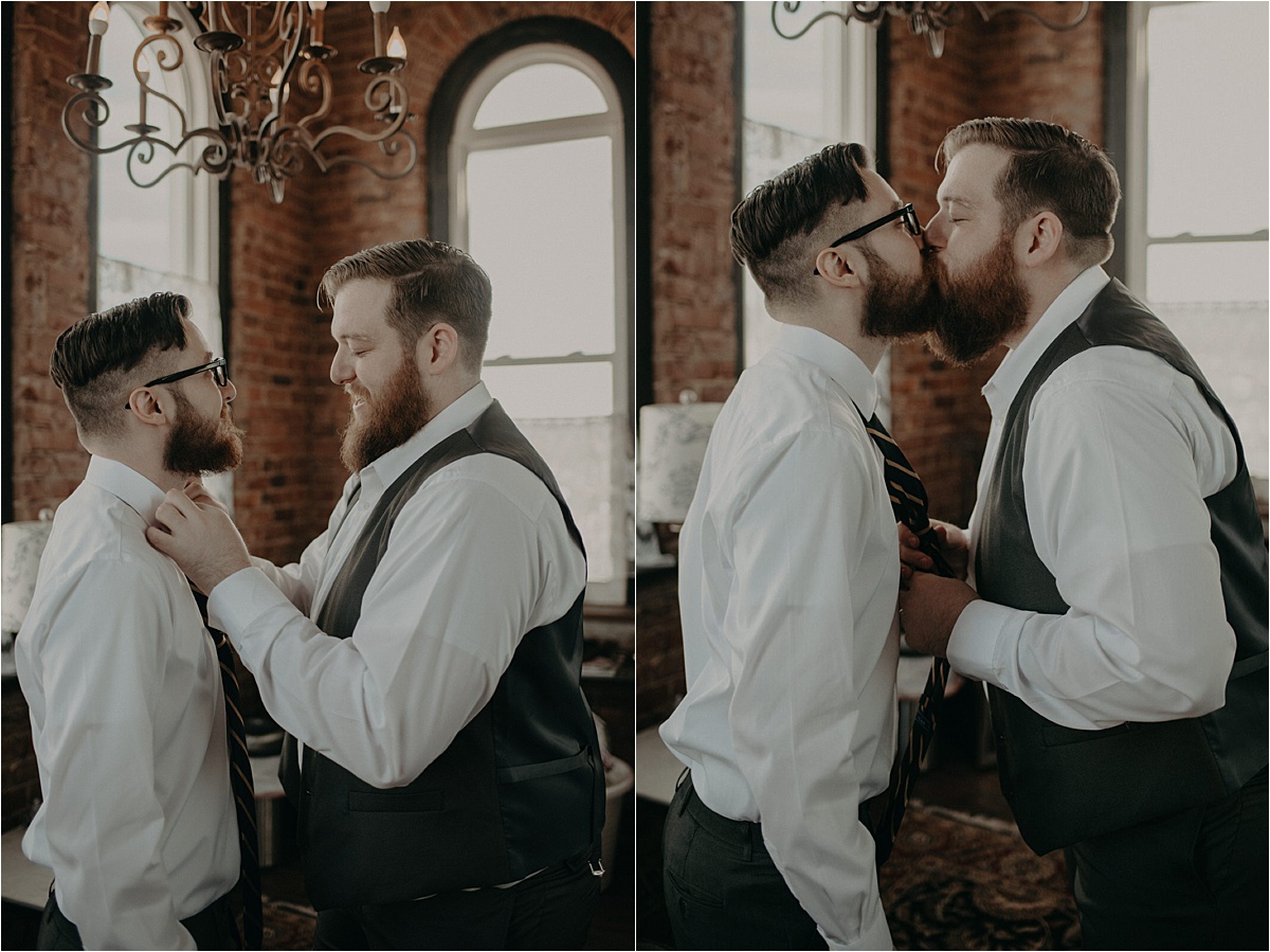 The grooms share a quick kiss as they help each other tie their neckties.
