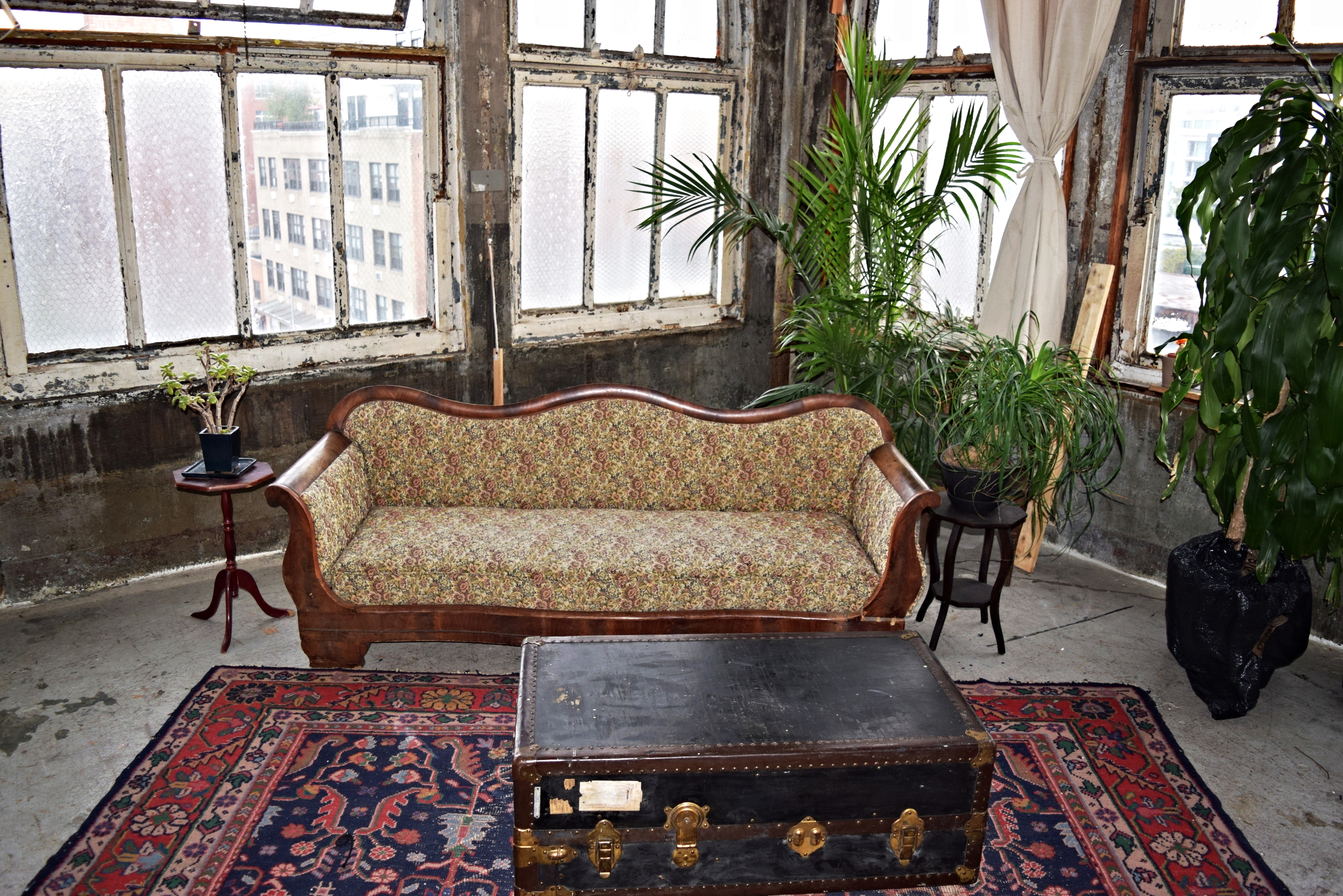 Vintage sofa, distressed Persian rug, steamer trunk, side tables and plants