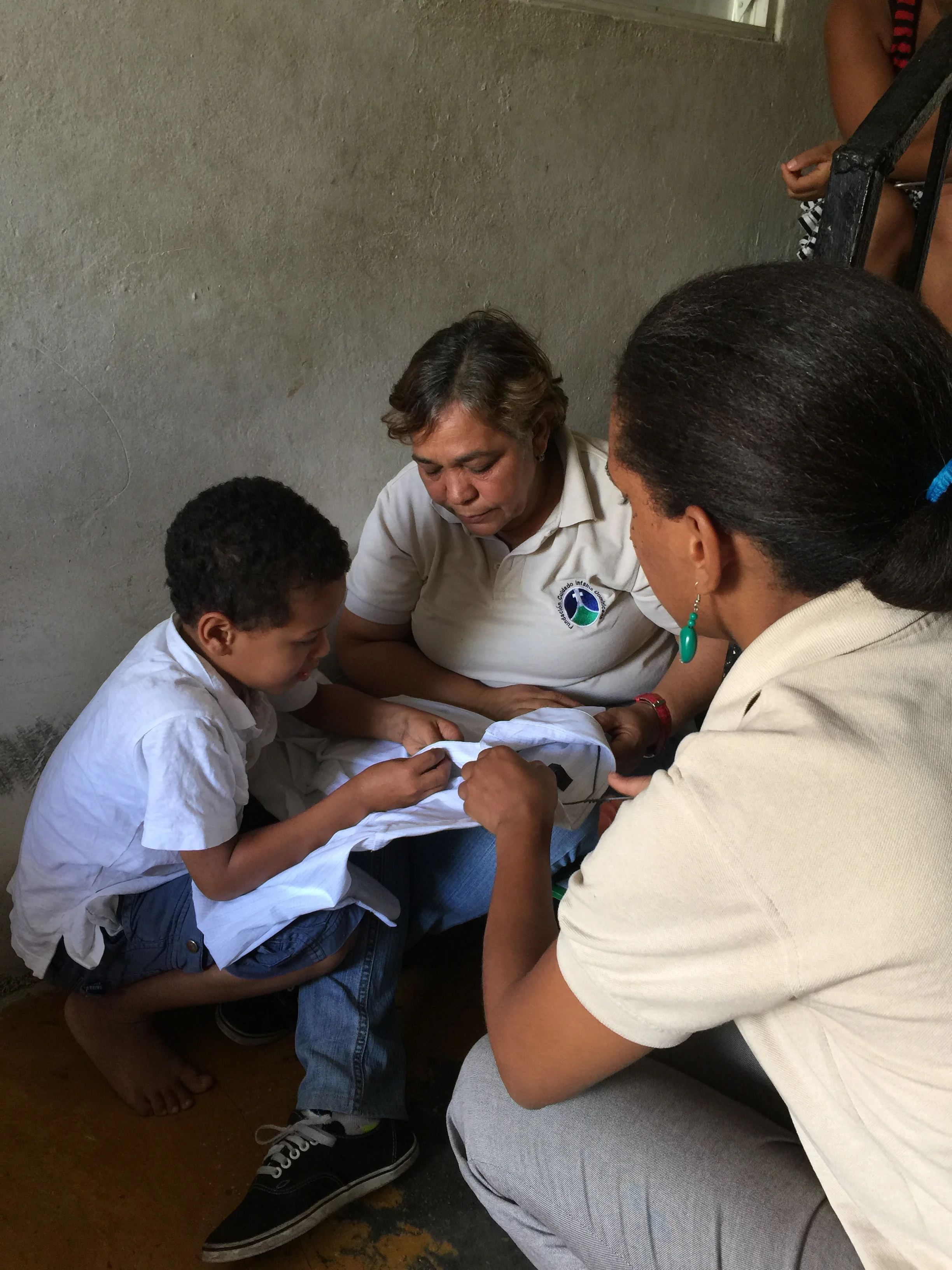 Jordy works on buttoning a shirt on a hangar with his promotoras.