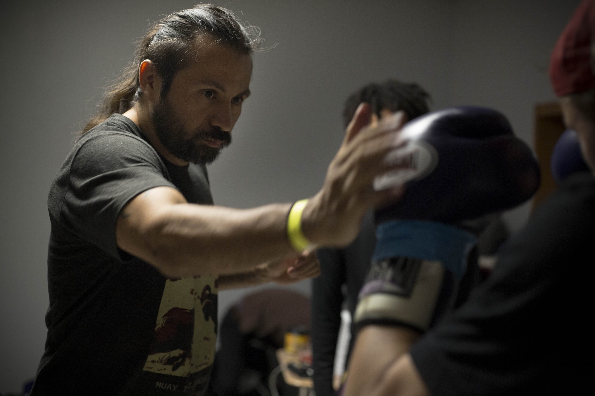 A man with long hair and a beard placing a padded helmet on a person's head during a training session.