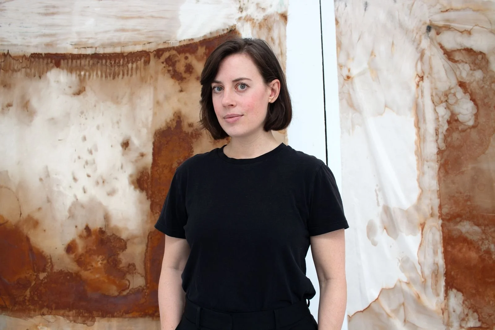 image of the artist standing in front of a large abstract work of art from the waist up, in a black t-shirt