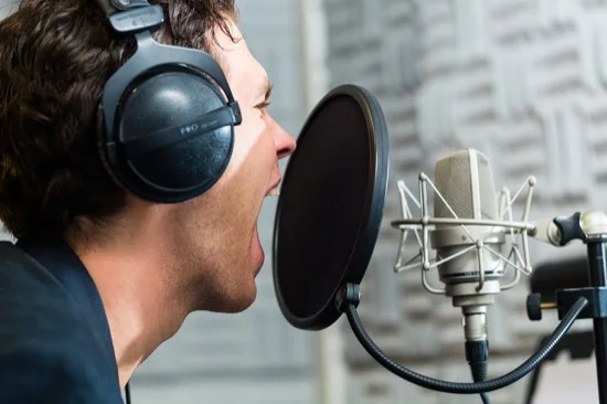 Young male singer or musician with microphone and headphone for audio recording in the Studio
