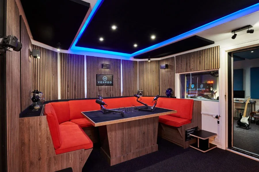 VOXPOD London podcast studio with red upholstered seating, microphones and control room