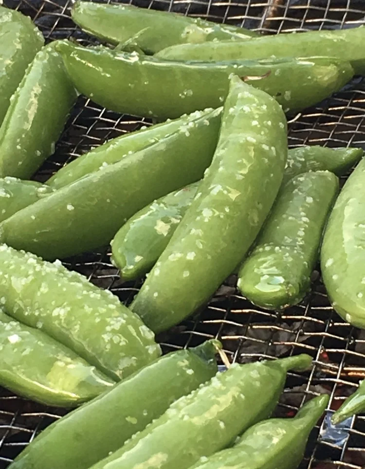 Blistered snap peas sizzling over hot coals.