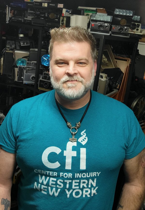 informal photo of Kenny Biddle, background electronic equipment, smiling, in green CFI t-shirt