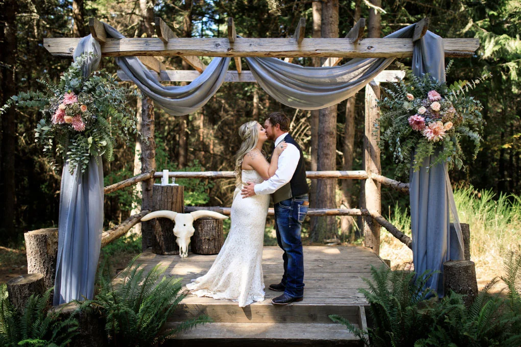  Bride and groom kissing at beautifully decorated country wedding altar. 