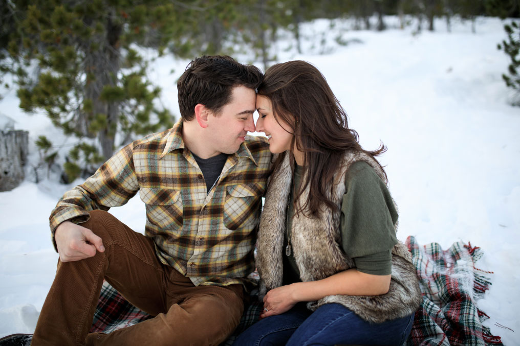 Man and woman nuzzling on a blanket in the snow.