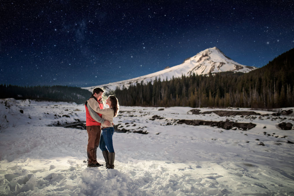 Dramatic image of man and woman embracing in front of snow covered mountain.