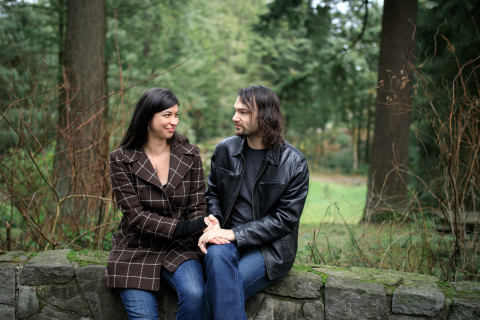  Man and woman sitting while smiling at each other and holding hands at a forest park. 