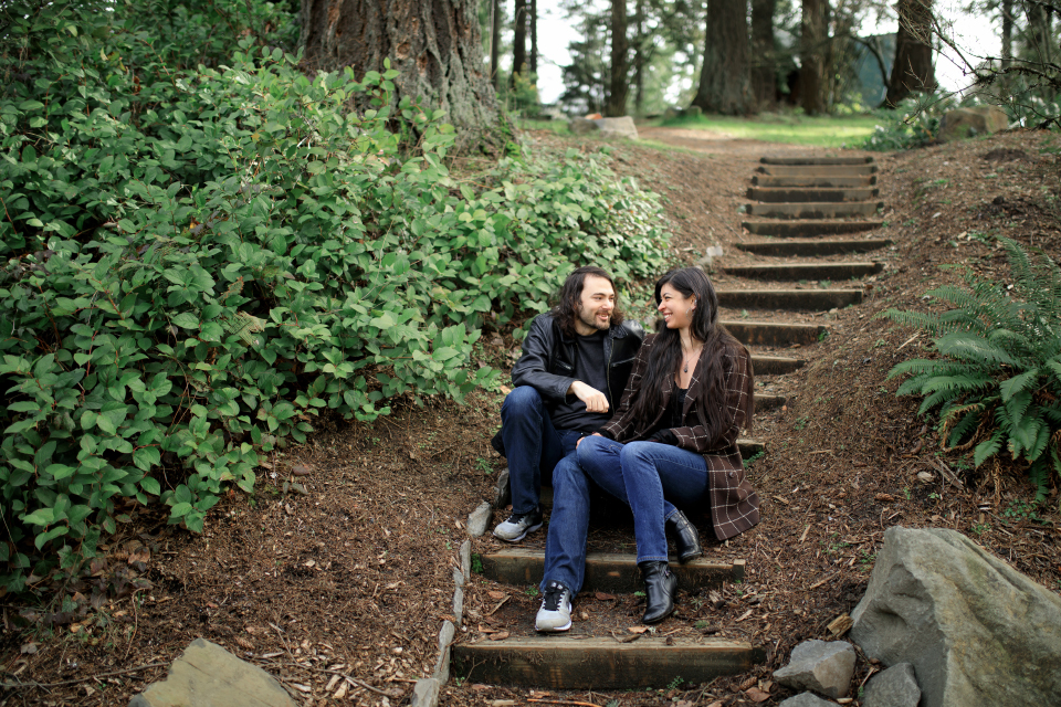  Man and woman sitting on stair steps smiling at each other in a forest park. 