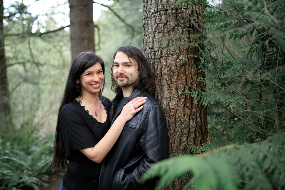  Man and woman smiling while leaning against a tree in the forest. 
