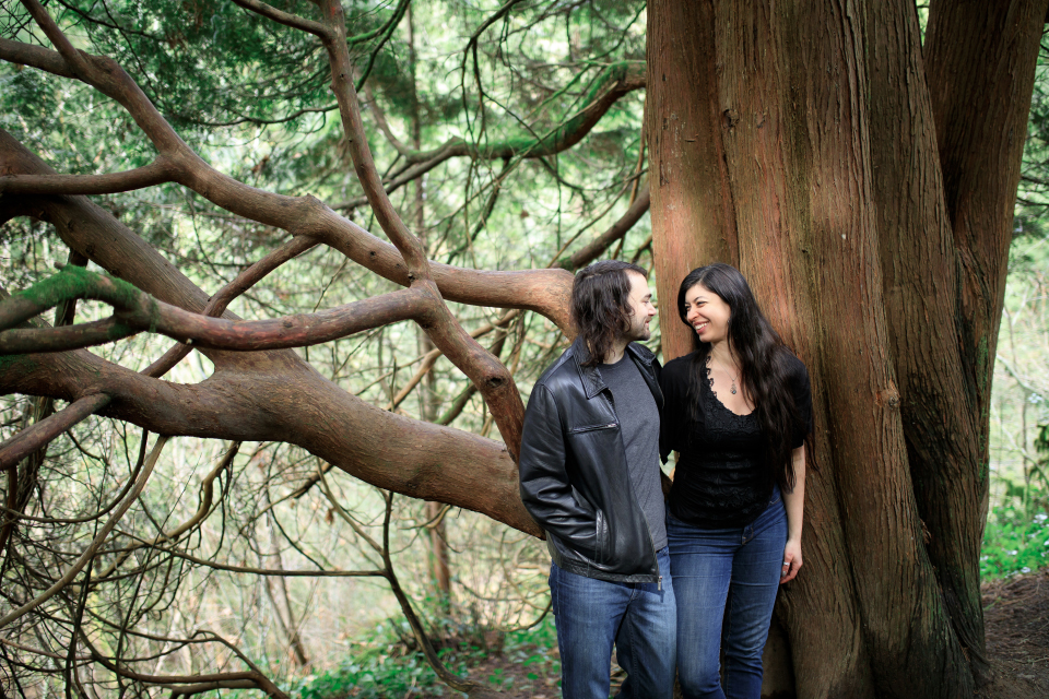  Man and woman smiling at each other while leaning against a tree. 